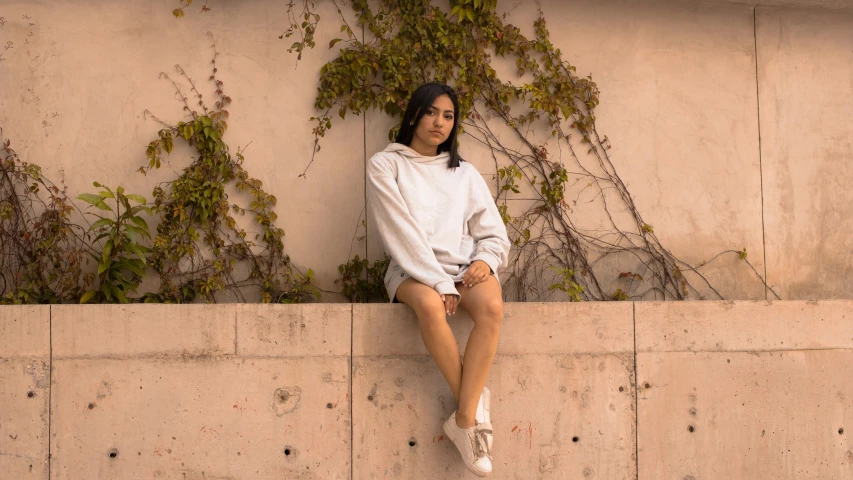 a woman sitting against a wall wearing white shoes