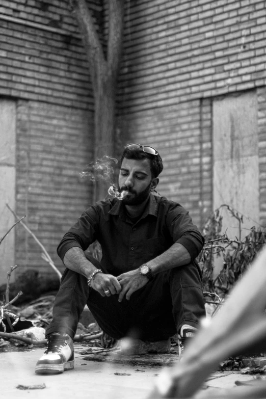 a man sits on the ground smoking a cigarette