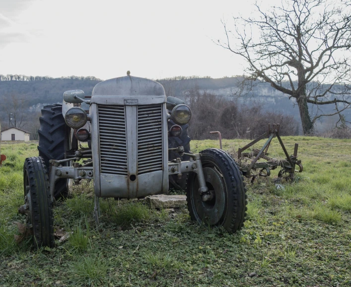 two men sit on an old tractor in a pasture