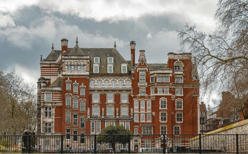 a red brick building with many windows and lots of clouds in the sky