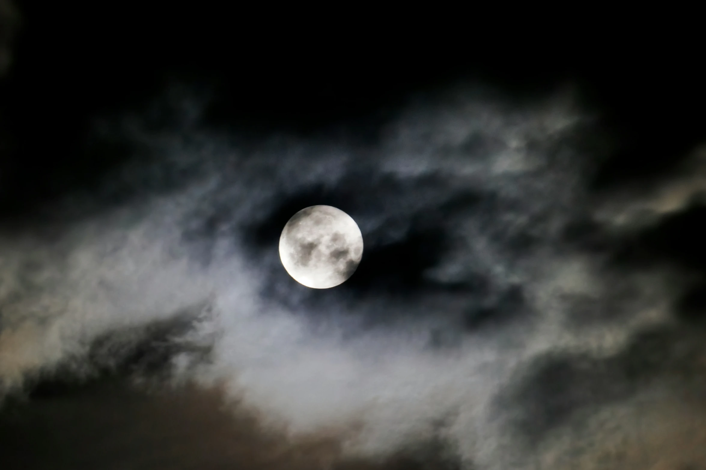 a full moon visible through a dark cloud sky