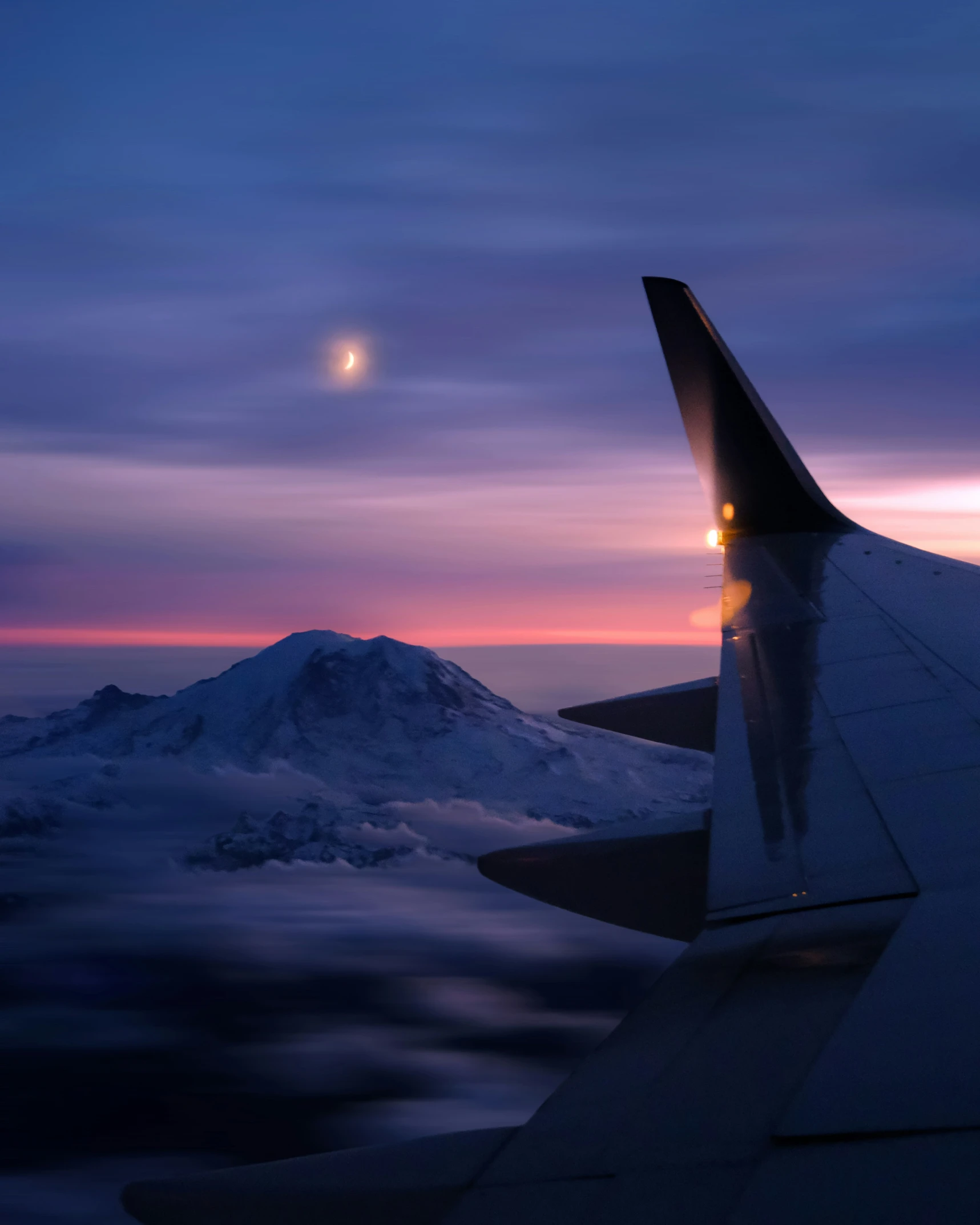 the sunset and moon are visible from above a plane wing