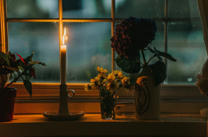 vases with flowers in front of a window lit by a candle