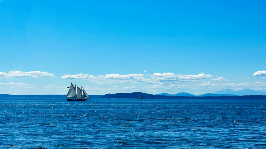 a sailboat sailing across the ocean in front of mountains