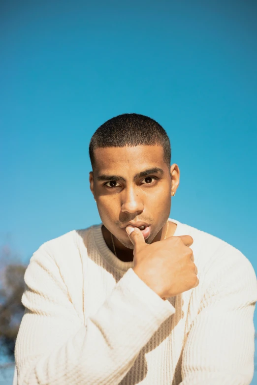 a man in a white sweater holding his hand near his lips