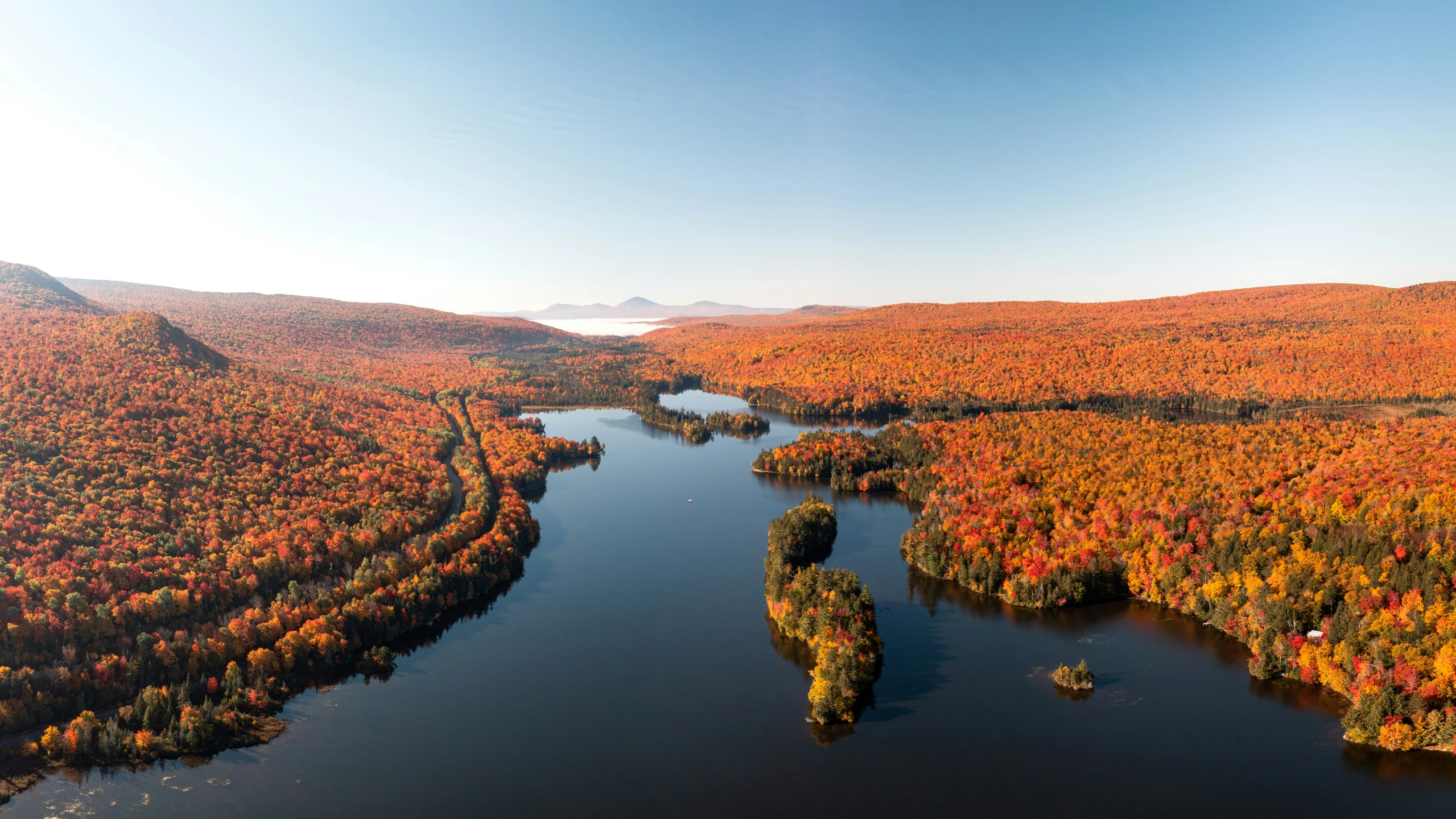 an aerial view of a river in the middle of a large wooded area with autumn colors