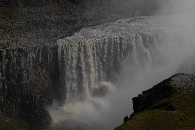 large waterfall on the side of a mountain near a river