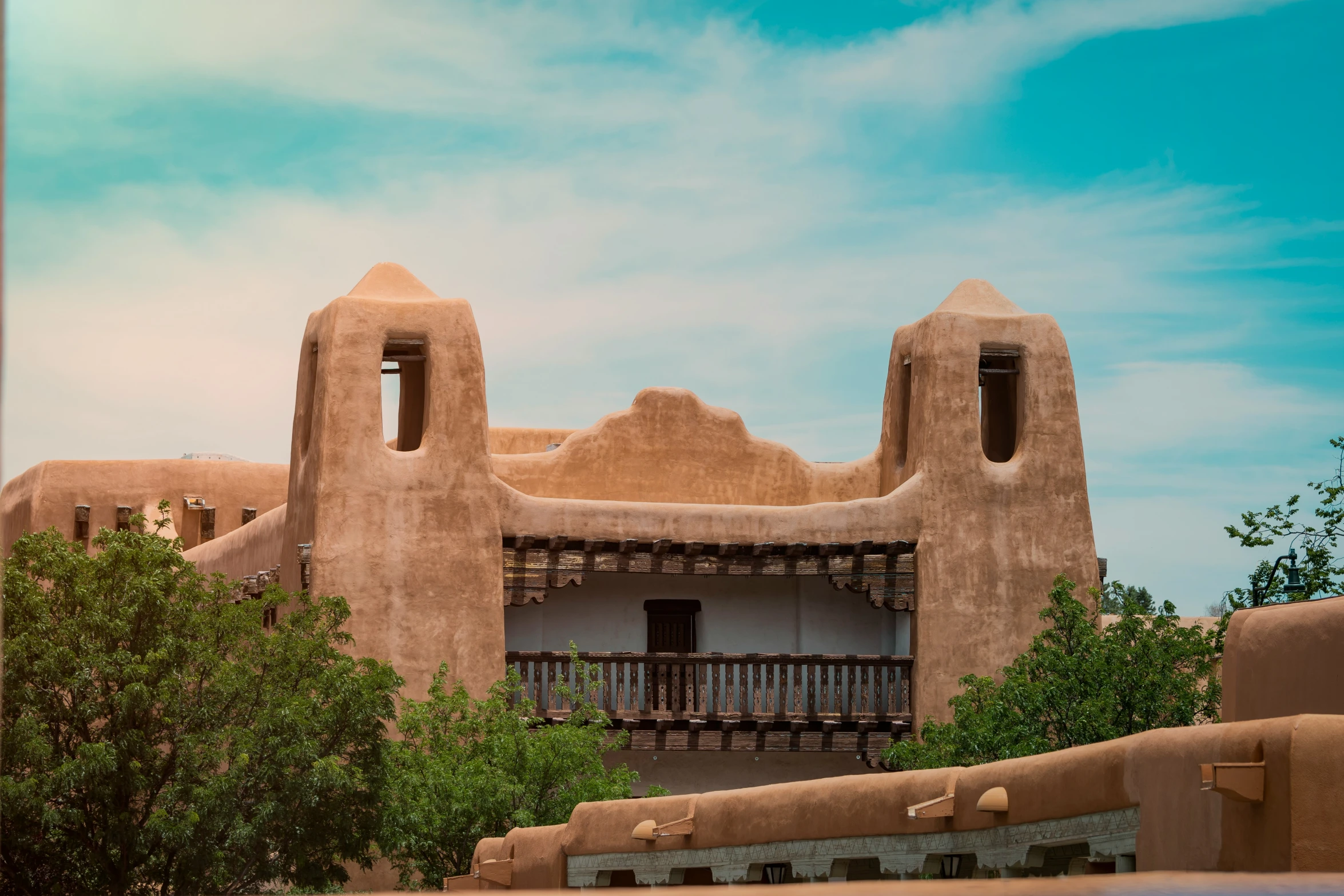 the adobe style home has a balcony and is surrounded by greenery