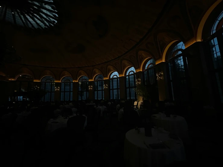 dark image of several tables in a room with several windows