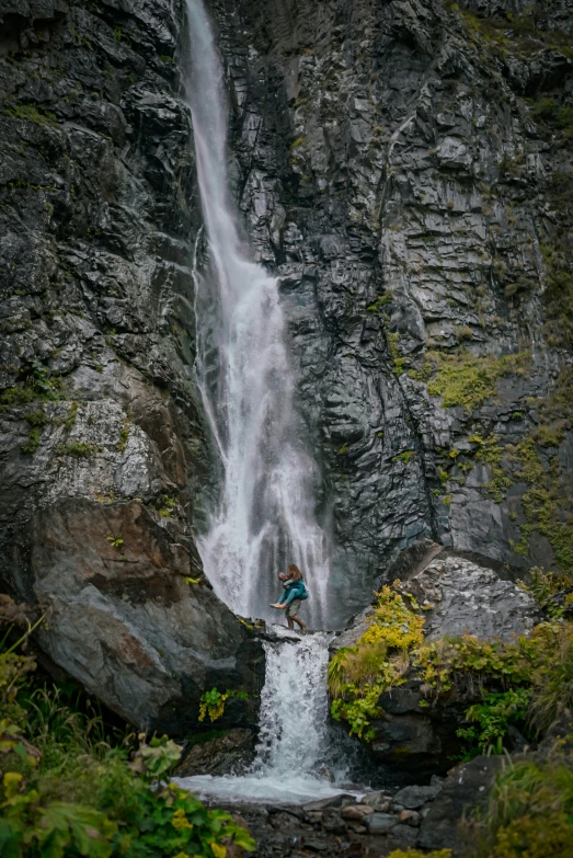 a person stands under a waterfall near large rocks