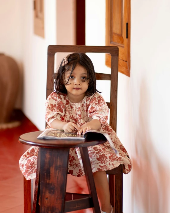 a girl in a red dress sitting on a chair with a book