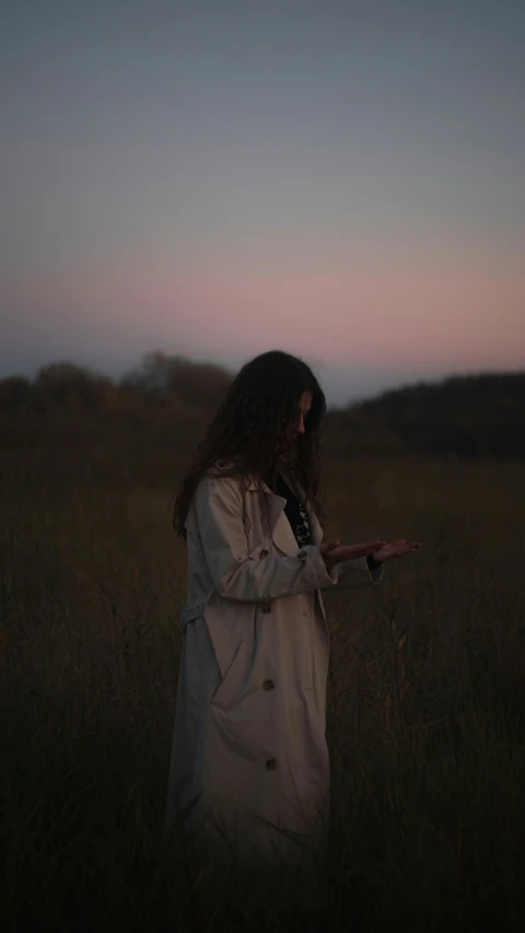 a woman standing in a field wearing a raincoat