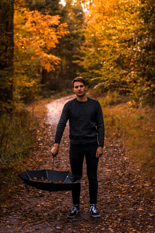 a young man standing in the woods holding a black umbrella