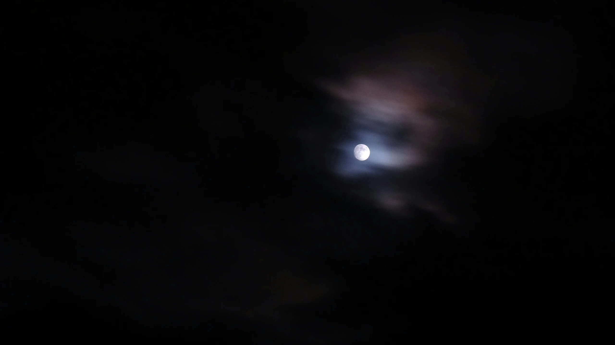 the moon is setting behind a cloud in the dark sky