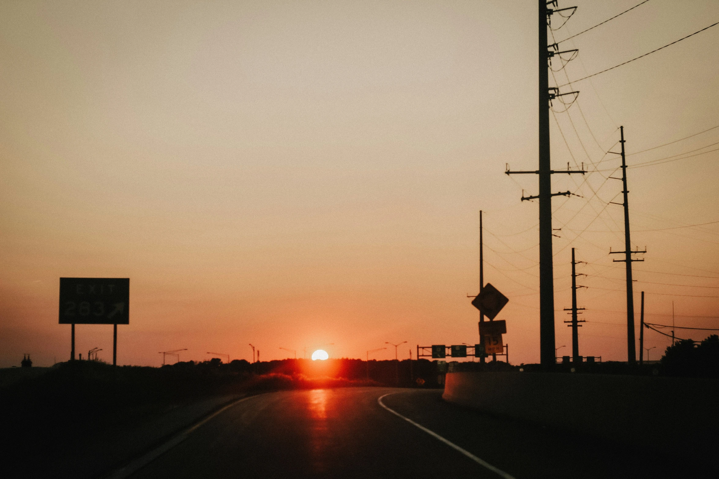 the sun is setting in the distance from a street sign