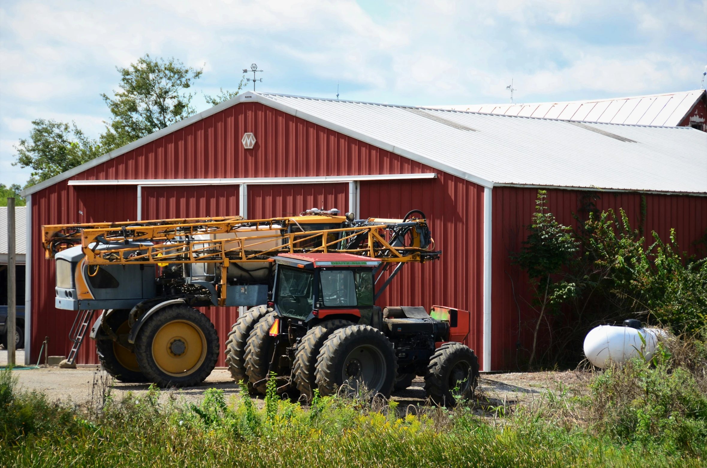 a truck near a red barn next to it is holding a ladder and lifting soing up