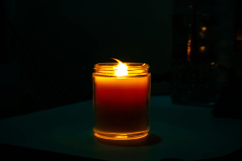 a lit candle sitting on a table next to a dark background