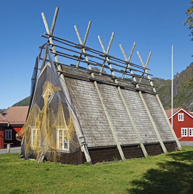 an old hut made out of sticks and logs in front of two red houses