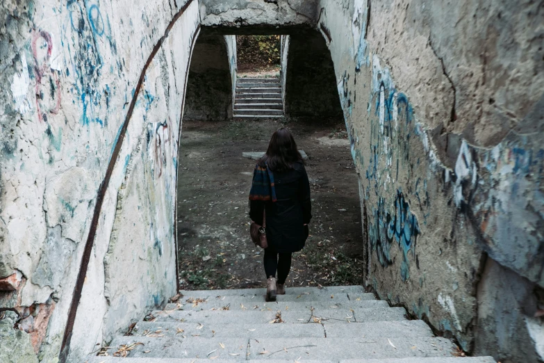 a woman in black jacket and scarf walking up some stairs