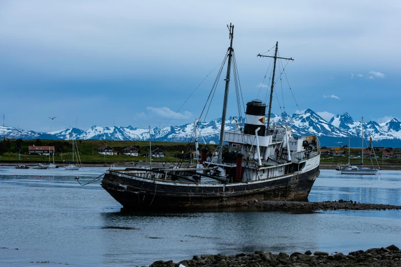 an old ship docked in the sea with mountains in the background