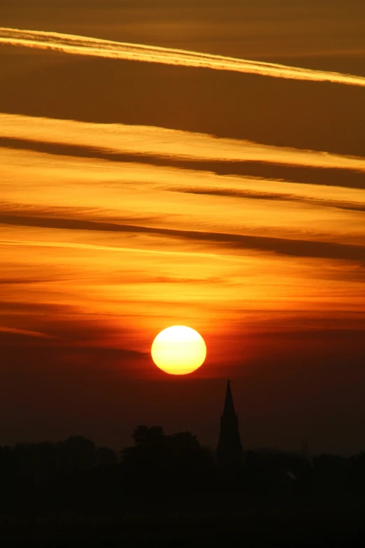 the sun rising over an old church steeple as seen from across the water