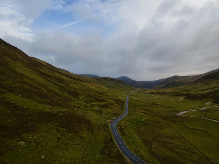 the sky is very cloudy and the road winding around the mountains