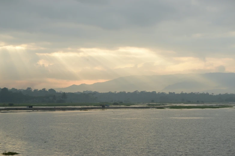 the sun shines through clouds over a calm river