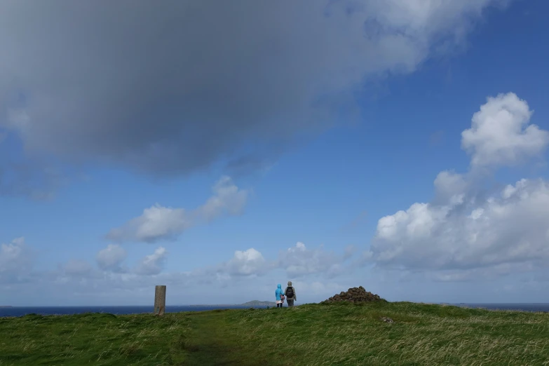 two people stand on the edge of a hill, with a small mound of dirt on one side of it