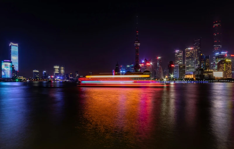 a very long boat traveling on a river in front of some tall buildings