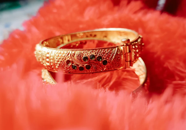 an ornate, gold celet, made out of gold and black stones, sits on a pink fan