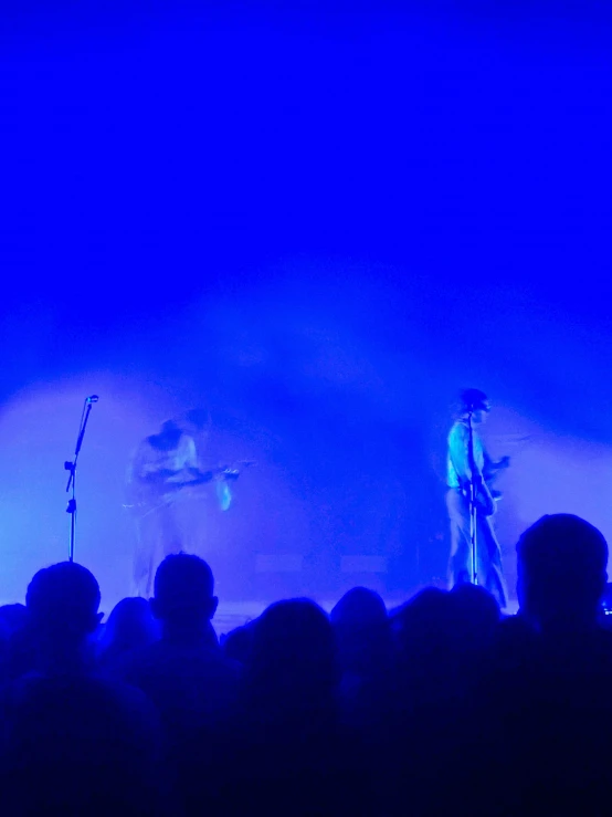 two people are on a stage, while a man in white and blue is at the back of the crowd