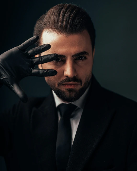 the man is dressed in black gloves and holding his hand over his forehead