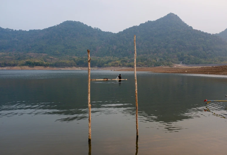 a single boat sits in the water next to two poles