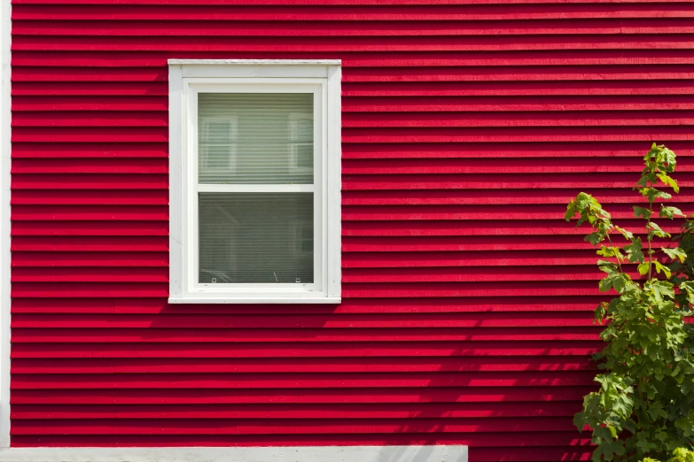 a red building with a white window and green bushes in front