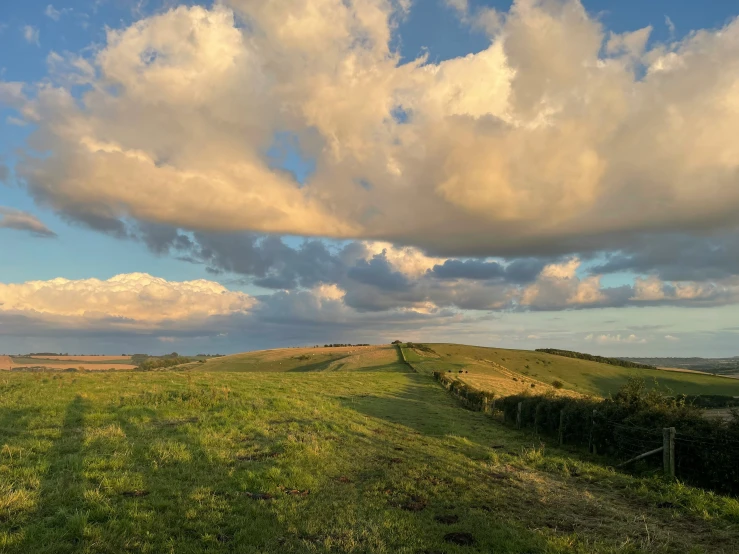 a view of clouds, green grass and mountains from the back