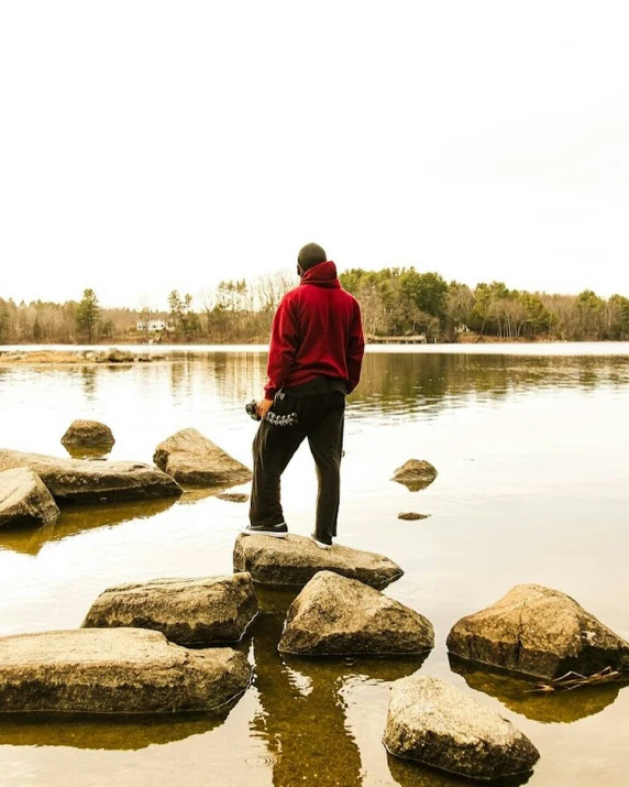 the man is standing on some large rocks at a lake
