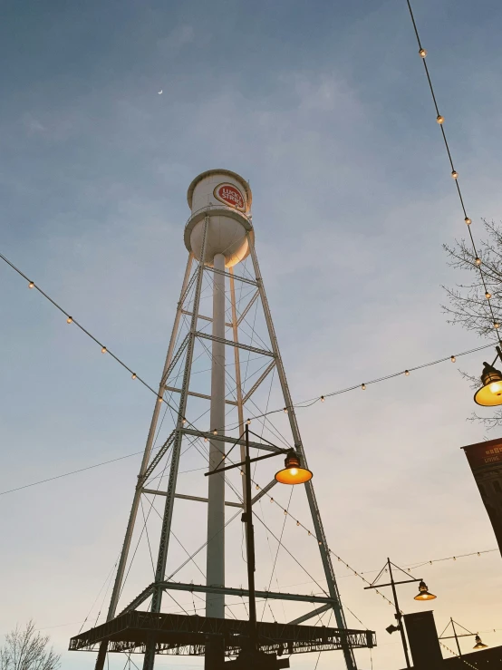 an old, metal water tower with lights on and buildings below