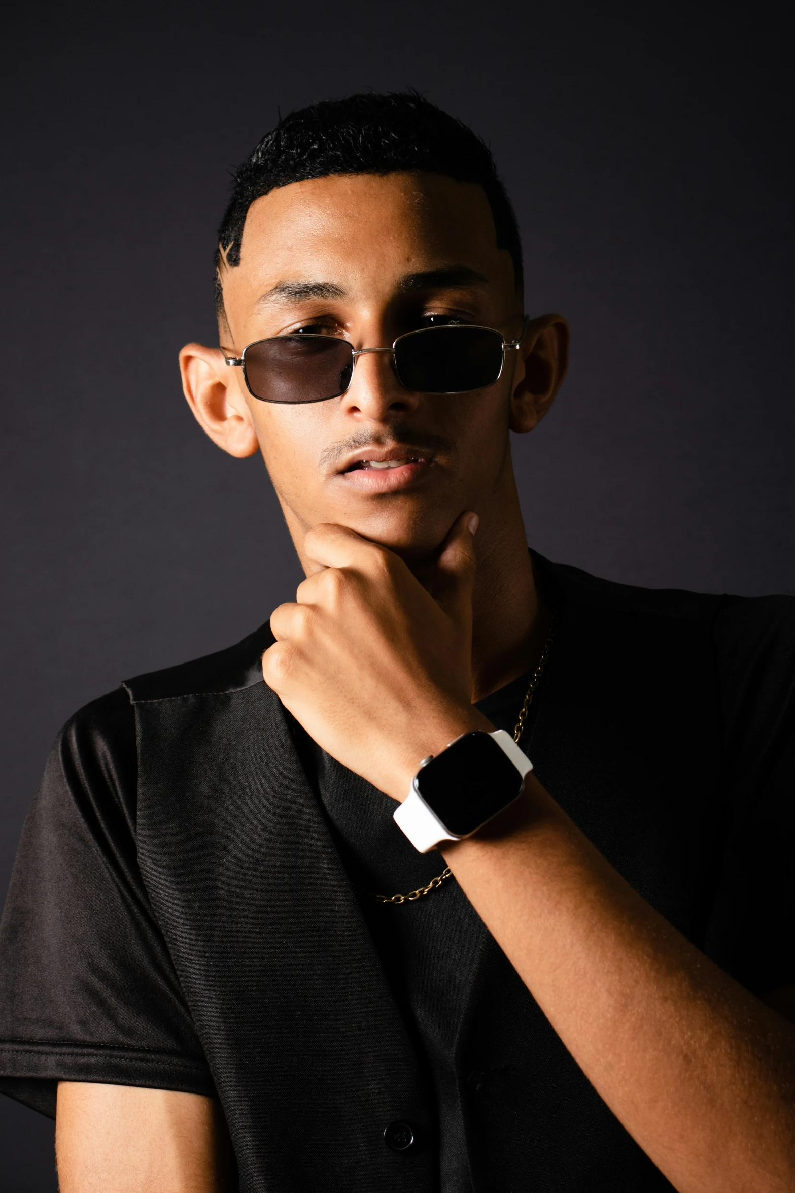 a young man wearing sunglasses standing in front of a dark background