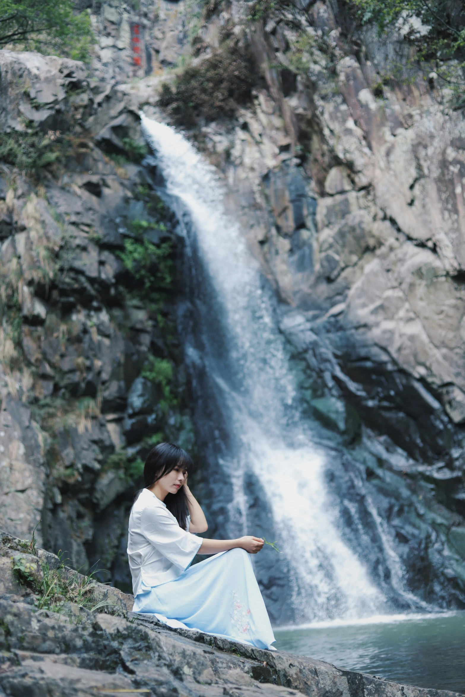 a woman sitting on a rock with a phone in front of a waterfall