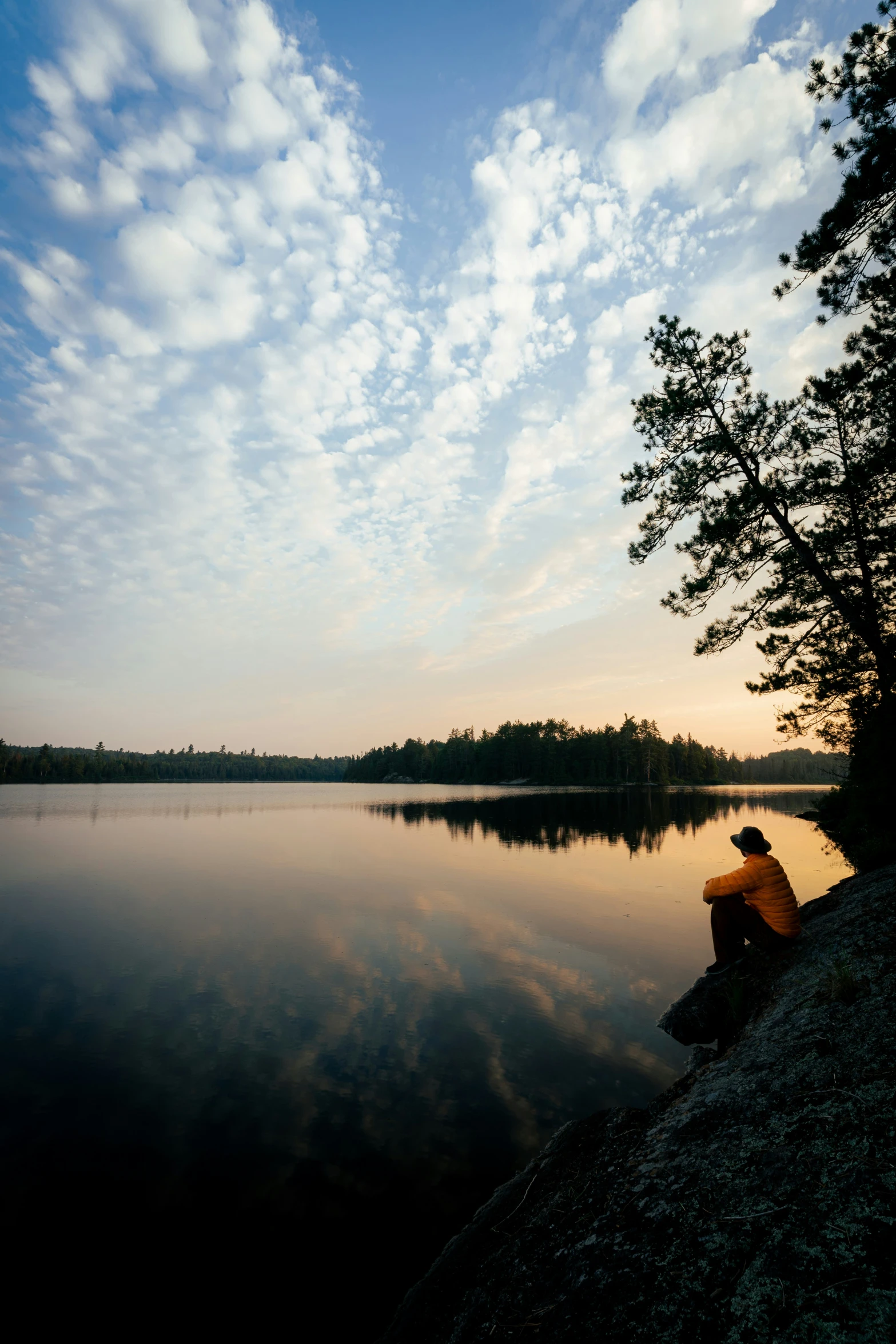 someone sitting on the rocks near a body of water with trees