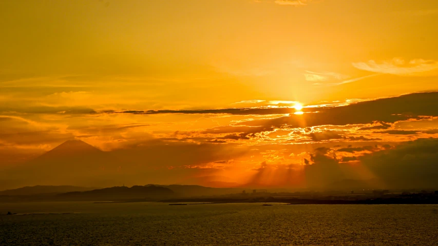 the sun setting over water with hills in the background