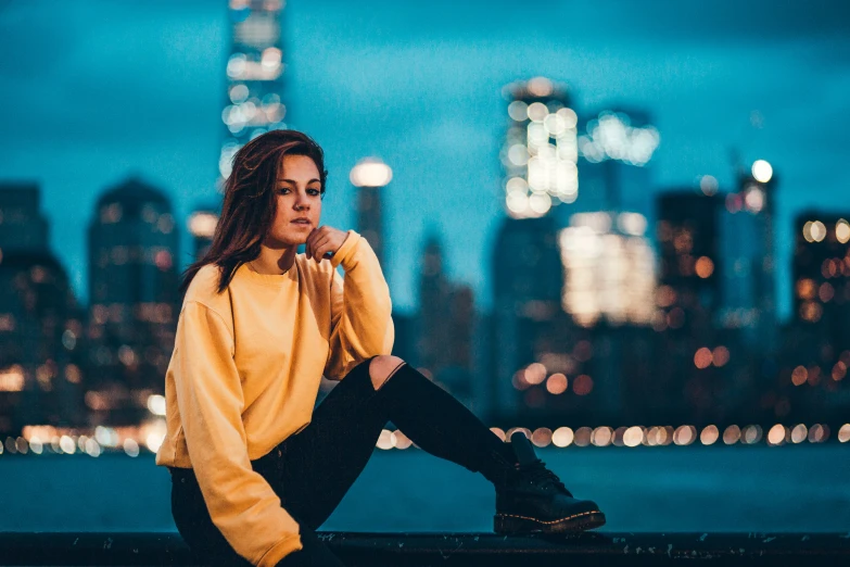 a woman posing on a ledge by the water with a view of a city