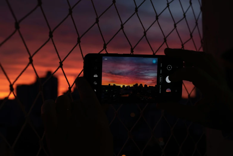 the hand is holding a camera up in front of a fence