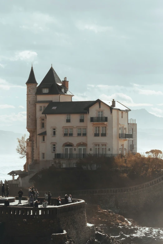 people stand near the edge of a cliff looking at an old castle