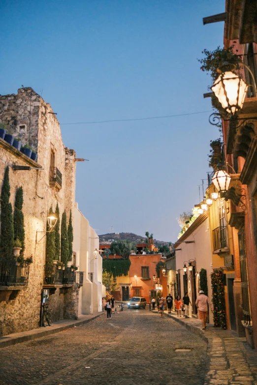 people walking down a cobblestone street at dusk