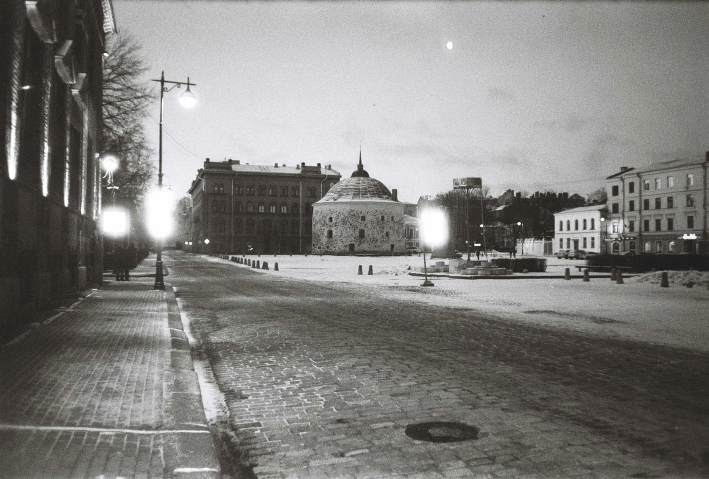 a snowy street has an ornate domed building and lamp posts