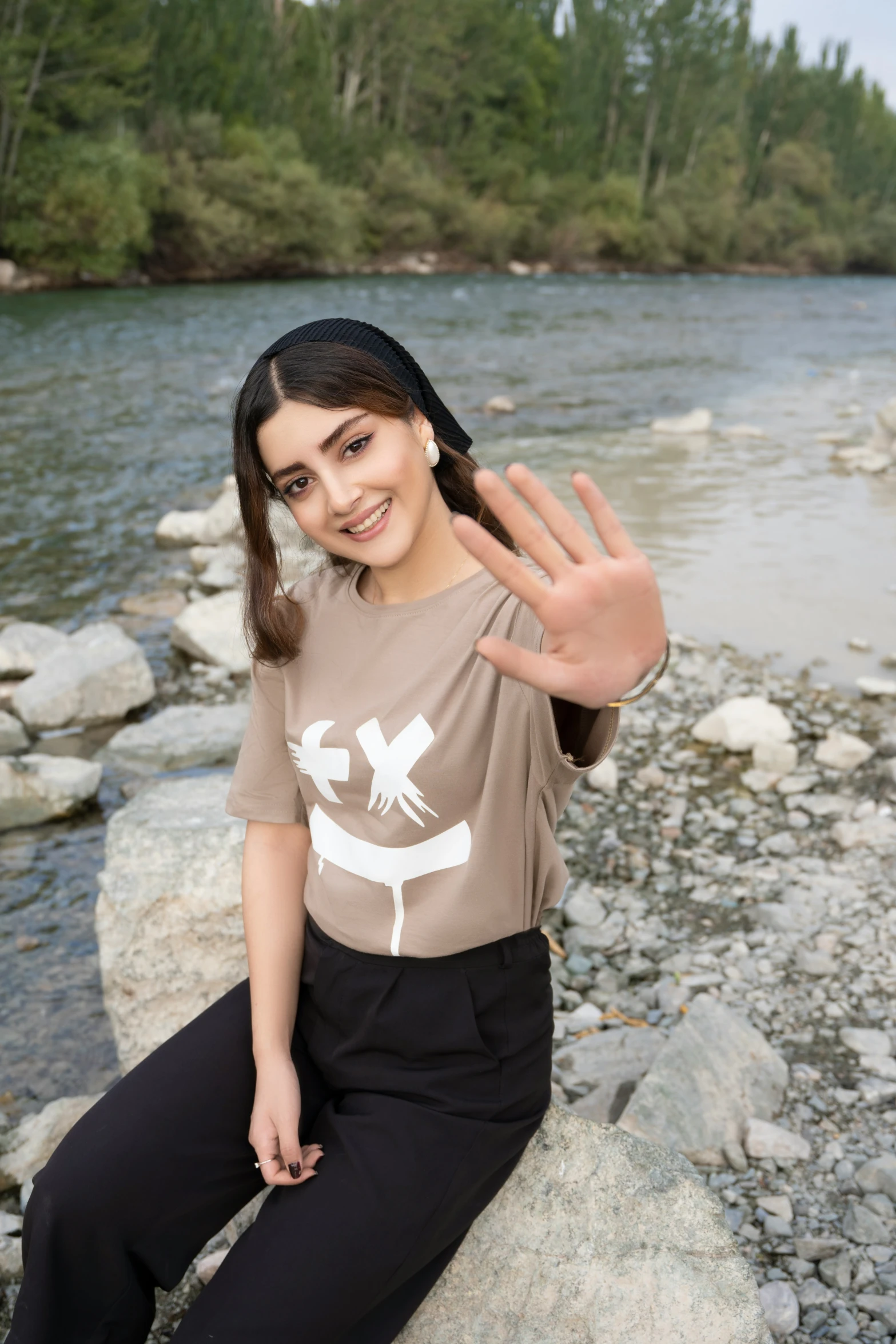 a  is smiling while sitting on rocks and waving