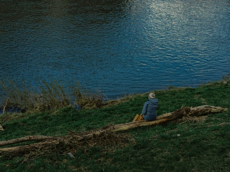 a man sitting on a log next to a river