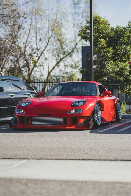 a red car parked on a parking lot next to a fence