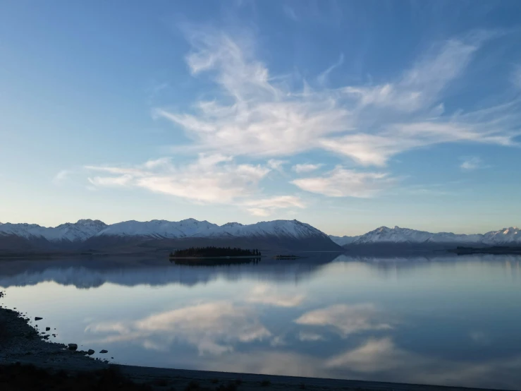 a lake surrounded by mountains and clouds in the sky